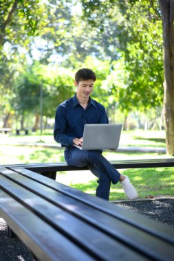 Parkta dizüstü bilgisayar kullanan mutlu Asyalı adam..