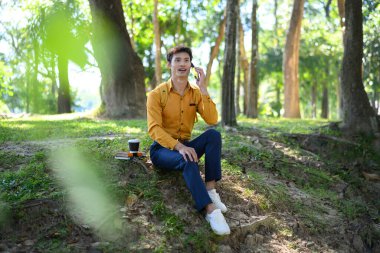 Ofisteki adam yeşil parkta oturmuş telefonla konuşuyor..