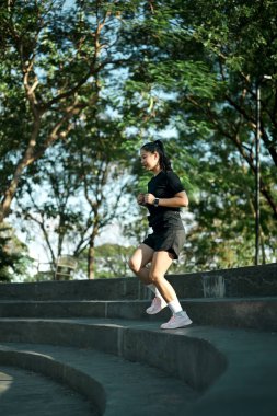 Kadın koşucu şehir parkında sabah ışıklarıyla idman yaparken beton merdivenlerden aşağı koşuyor..