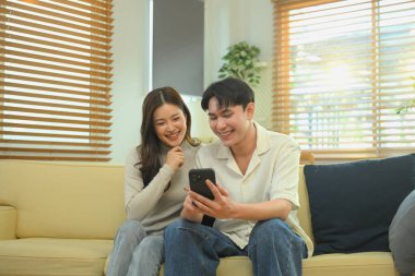 Genç çift kanepede dinleniyor, Sevgililer Günü 'nde akıllı telefonlarıyla internetten alışveriş yapıyorlar..