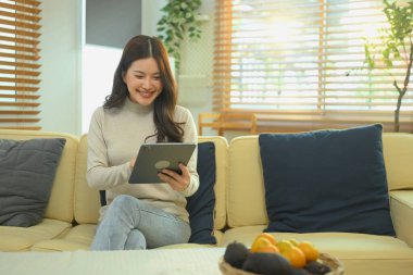 Kanepede oturan bir kadın tablet ve internet bağlantısı kullanarak gülümsüyor. Mutlu teknoloji keyfi..