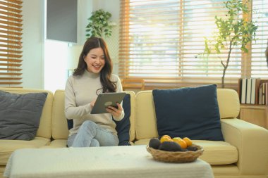 Kanepede oturan bir kadın tablet ve internet bağlantısı kullanarak gülümsüyor. Mutlu teknoloji keyfi..