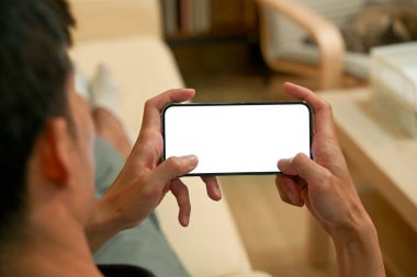 Oturma odasındaki kanepede uzanırken akıllı telefon boş ekran modern tasarım kullanan bir adam..