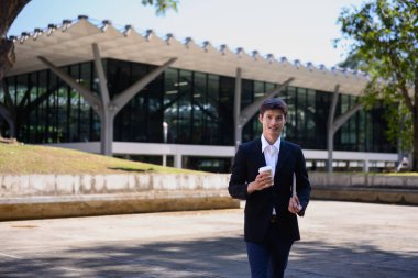 Ofisten bir adam elinde bir laptop ve kahve fincanı ile dışarı çıkıyor..