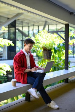 Profesyonel bir adam, modern bir binanın dışında dizüstü bilgisayarla çalışmaya odaklanmış..