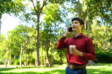 Parlak yeşil bir parkta telefonla konuşan adam..