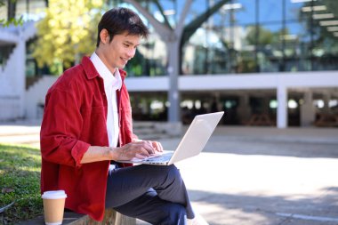 Profesyonel bir adam, modern bir binanın dışında dizüstü bilgisayarla çalışmaya odaklanmış..