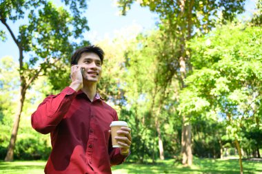 Parlak yeşil bir parkta telefonla konuşan adam..