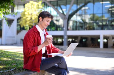 Profesyonel bir adam, modern bir binanın dışında dizüstü bilgisayarla çalışmaya odaklanmış..