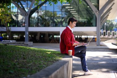 Profesyonel bir adam, modern bir binanın dışında dizüstü bilgisayarla çalışmaya odaklanmış..