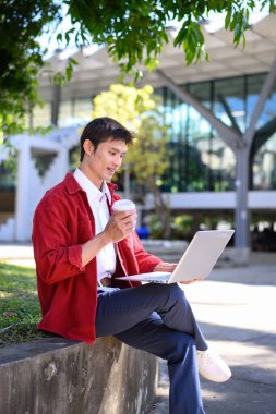 Profesyonel bir adam, modern bir binanın dışında dizüstü bilgisayarla çalışmaya odaklanmış..