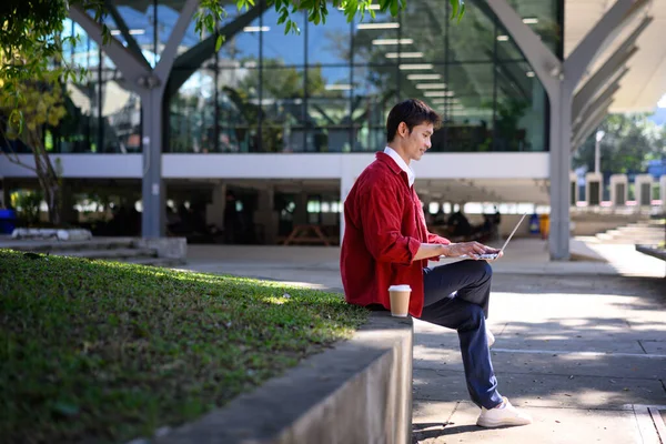 Profesyonel bir adam, modern bir binanın dışında dizüstü bilgisayarla çalışmaya odaklanmış..