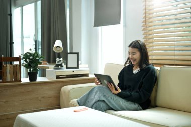 A young woman relaxing on a sofa using a tablet at home, enjoying a calm holiday mood with comfort and leisure time.