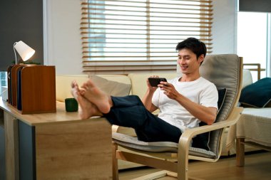 Cep telefonuyla oyun oynayan ve koltukta oturan bir adam..