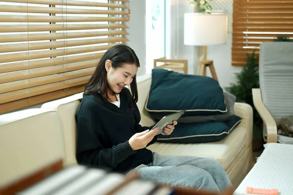 Genç bir kadın evinde tablet kullanarak kanepede dinleniyor, rahat ve sakin bir tatil havasının tadını çıkarıyor..