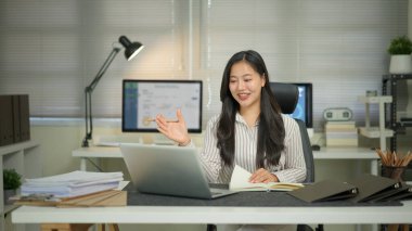 Asyalı bir kadın bilgisayarını kullanarak uzaktan kumandalı ekibiyle görüntülü görüşme yapıyor..