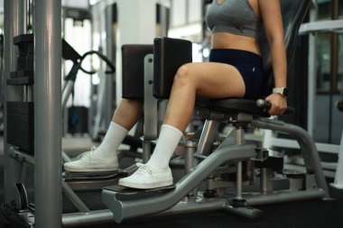 Kırpılmış vurulan kadın, antrenörü aktiviteleri kaydederken iç kalça makinesinde çalışıyor..