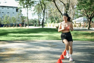 Hız ve çeviklik konisi tatbikatı yapan bir kadın açık havada egzersiz yapıyor..
