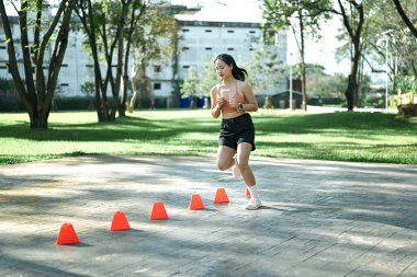 Hız ve çeviklik konisi tatbikatı yapan bir kadın açık havada egzersiz yapıyor..
