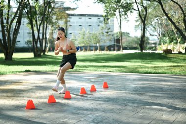Hız ve çeviklik konisi tatbikatı yapan bir kadın açık havada egzersiz yapıyor..