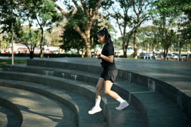 Kadın koşucu şehir parkında sabah ışıklarıyla idman yaparken beton merdivenlerden aşağı koşuyor..