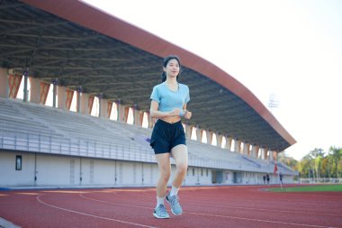 Genç Asyalı kadın sabah egzersizi için stadyumda koşuyor..