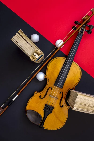 Kırmızı-siyah arka planda keman, yay ve kitaplar, üst görünüm