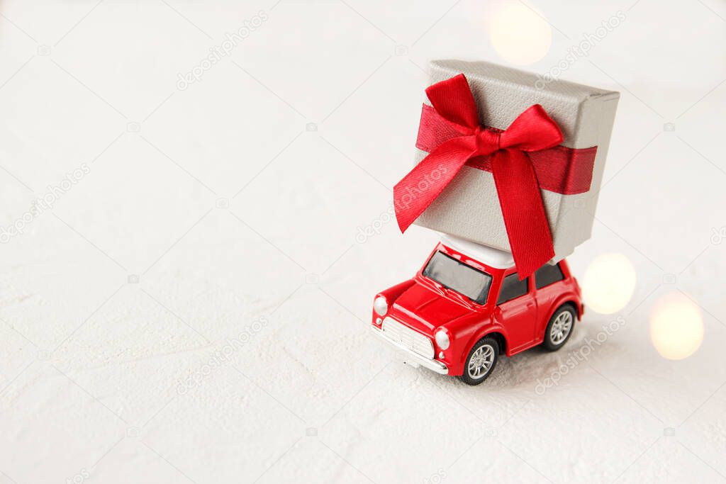 Red toy car delivering Christmas or New Year gifts on white background. Christmas greeting card concept. Close up.