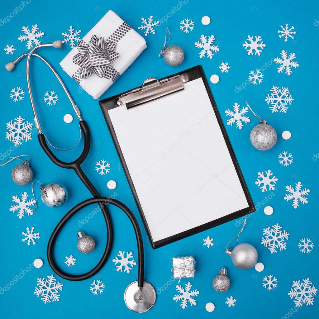 Christmas, medicine greeting card. Blank clipboard and Christmas decorations, pills on a blue background. Medical concept. Copy space, flat lay