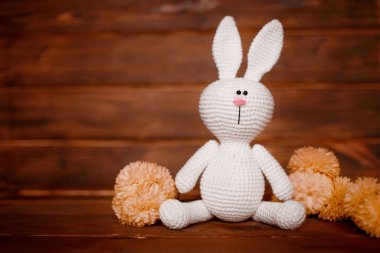 Ahşap arka planda çiçekli el yapımı amigurumi tavşanı. Bebek geçmişi. Boşluğu kopyala.