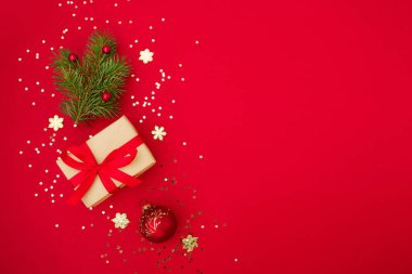 Noel kompozisyon tebrik kartı. Kırmızı arka planda altın yıldızlı konfeti ve Noel süslemesi olan el sanatları kağıdından hediyeler. Üst manzara, düz uzanma