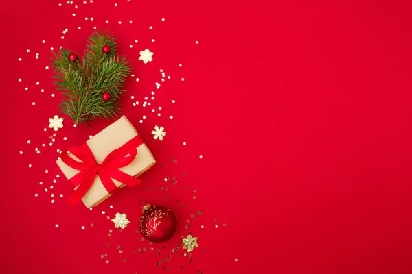 Noel kompozisyon tebrik kartı. Kırmızı arka planda altın yıldızlı konfeti ve Noel süslemesi olan el sanatları kağıdından hediyeler. Üst manzara, düz uzanma