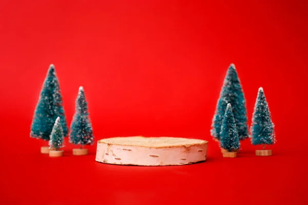 Ahşap bir podyum ile son moda kırmızı arka plandaki ahşap bir çember ve noel süsleme ağacı oluşturun. Yılbaşı ürünü sunumu için yer.