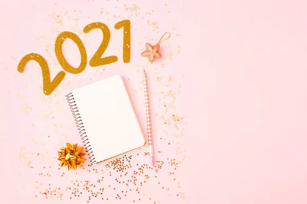 Yeni yıl hedef listesi 2021. Yıldız konfetisiyle birlikte pembe pastel arka plan üzerine kurulu yeni yıl hedeflerini ve kararlarını listelemek için defterli bir masa. Değişim ve kararlılık kavramı