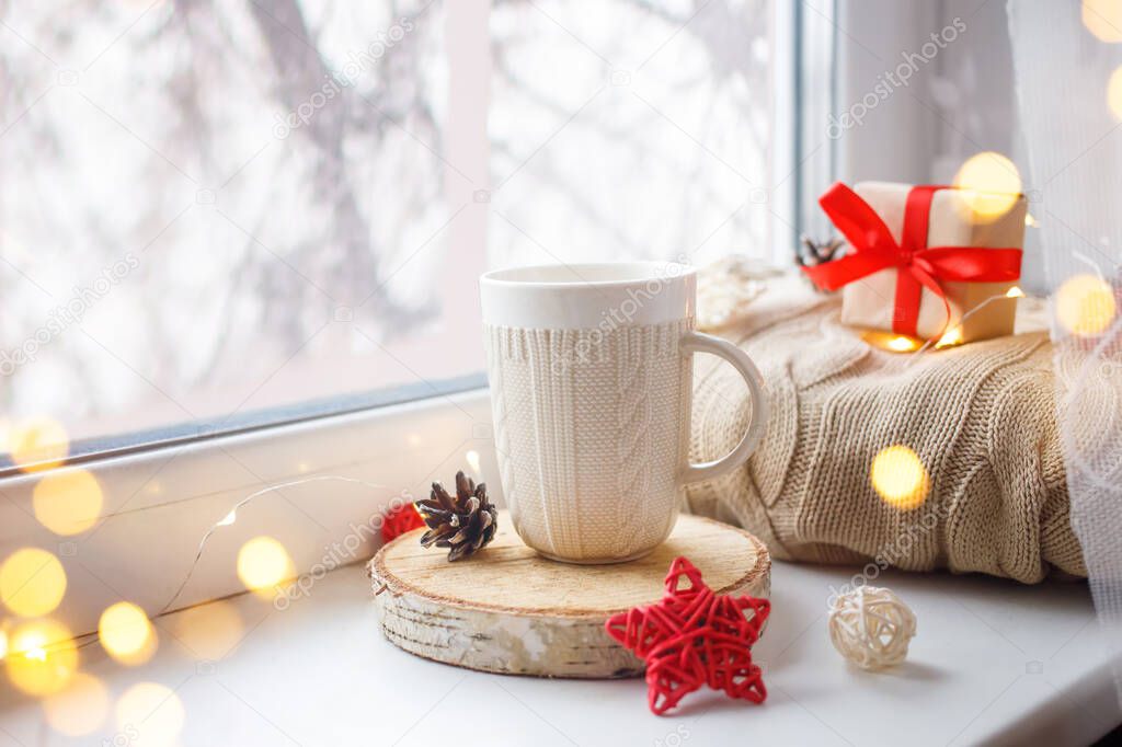 Hot tea, coffee. Winter background with cup of coffee, tea, on the window, knitted scarf and gift. Christmas greeting card concept.