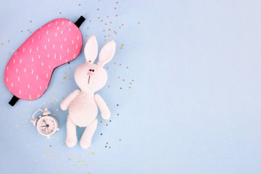 Sağlıklı uyku konsepti. Alarmlı tavşan ve konfeti yıldızlı mavi bir arka planda uyku maskesi. Üst görünüm, düz görünüm, kopyalama alanı.