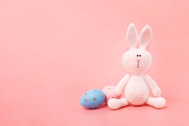 Paskalya kartı konsepti. Pembe pastel arka planda Paskalya yumurtaları olan el yapımı Amigurumi tavşanı. Boşluğu kopyala.