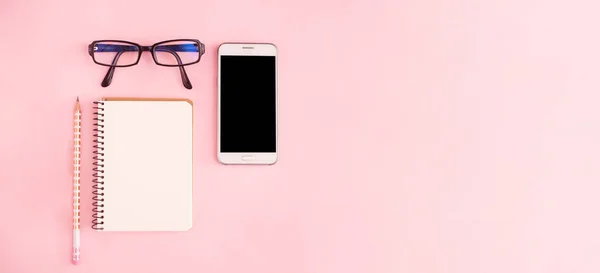 Bureau à domicile avec smartphone, bloc-notes, lunettes sur fond rose pastel. Espace de travail indépendant ou concept d'entreprise à domicile. Pose plate, vue du dessus, espace de copie, bannière. — Photo