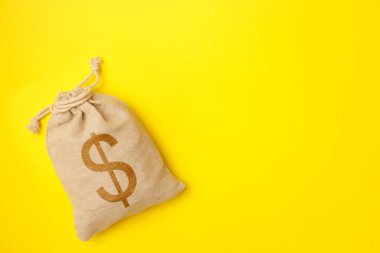 Sarı arka planda bir torba bozuk para ve bir dolar işareti. Mali ve yatırımları koruma kavramı. Üst görünüm, düz görünüm, kopyalama alanı.