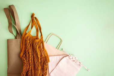 Asma ipli çantalar, doğal pamuk kumaştan yapılmış küçük eko çuvalların maketi, yukarıdan bakıldığında yeşil pastel arka planda yatıyordu.