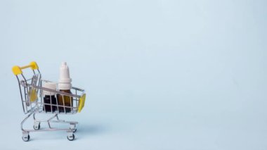 Mavi arka plandaki alışveriş arabasındaki ilaç ve hapların hareketini durdur. Uyuşturucu teslimatı. Boşluğu kopyala