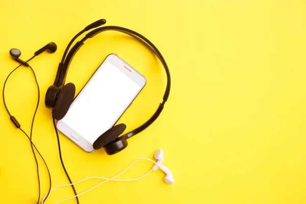 Sarı arka planda kulaklık ve akıllı telefon. Kulüp sosyal medya konsepti. Model yap, boşluğu kopyala, düz yat, üst görünüm