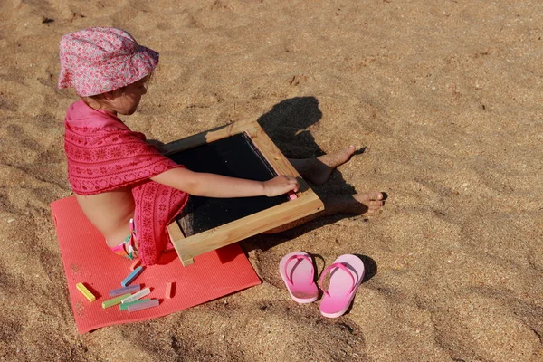 Cute Little Girl Beach Sitting Sand Draws Blackboard Chalk Hot — Stock Photo, Image