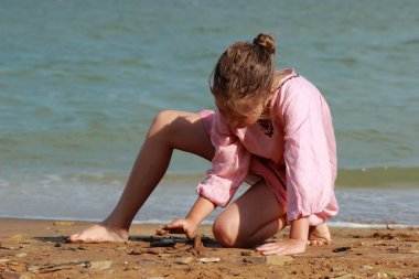 güzel küçük kız hafif pembe elbise giyen ve çakıl ile sahil üzerinde oynama