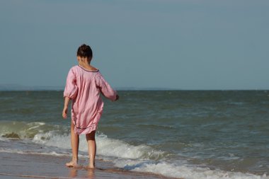 güzel küçük kız hafif pembe elbise giyen ve çakıl ile sahil üzerinde oynama