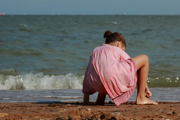 漂亮的小女孩穿着淡粉色裙子和在海边玩小石头 — 图库照片
