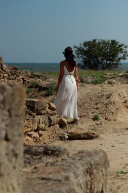 Yunan tarzı uzun beyaz elbiseli tatlı genç kız antik şehir Nymphaeum 'un kazı alanına gidiyor, Kerch.