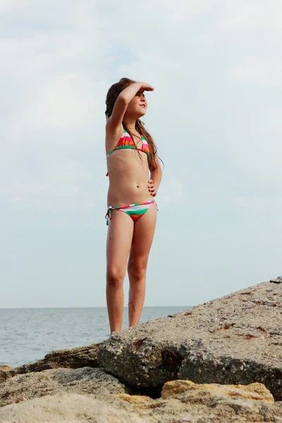 海背景と青空のビーチで大きな岩に水着立っているテーマ夏休みの旅行で幸せな少女 — ストック写真