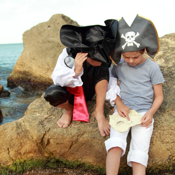 悲しい少年と海賊コスチュームや海辺での大きな岩の上に座って美しい海賊帽子の少女 — ストック写真
