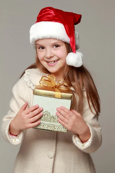 Söt leende liten flicka i tomtens röda hatt hålla jul box — Stockfoto